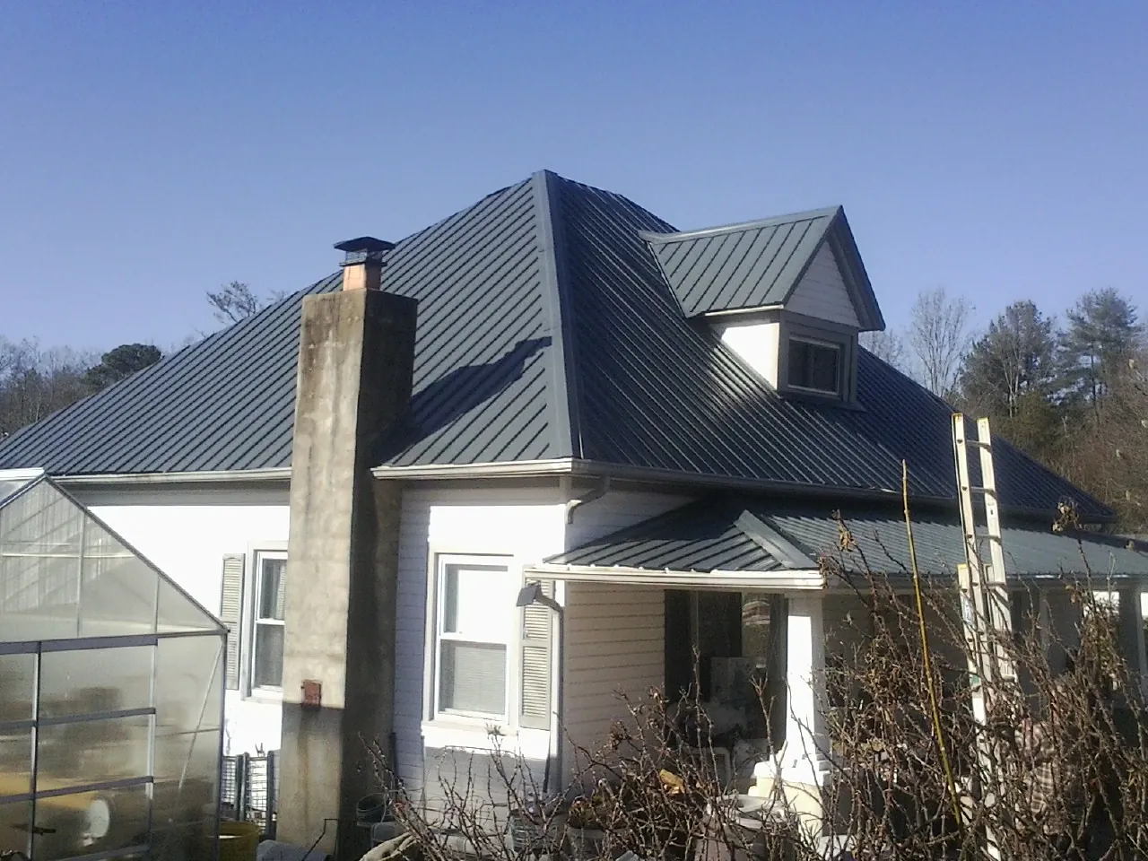 Dark blue standing seam metal roof on a white farmhouse with dormer — Slate & Tile Roof Repair by Roofing Brothers in Lake Junaluska