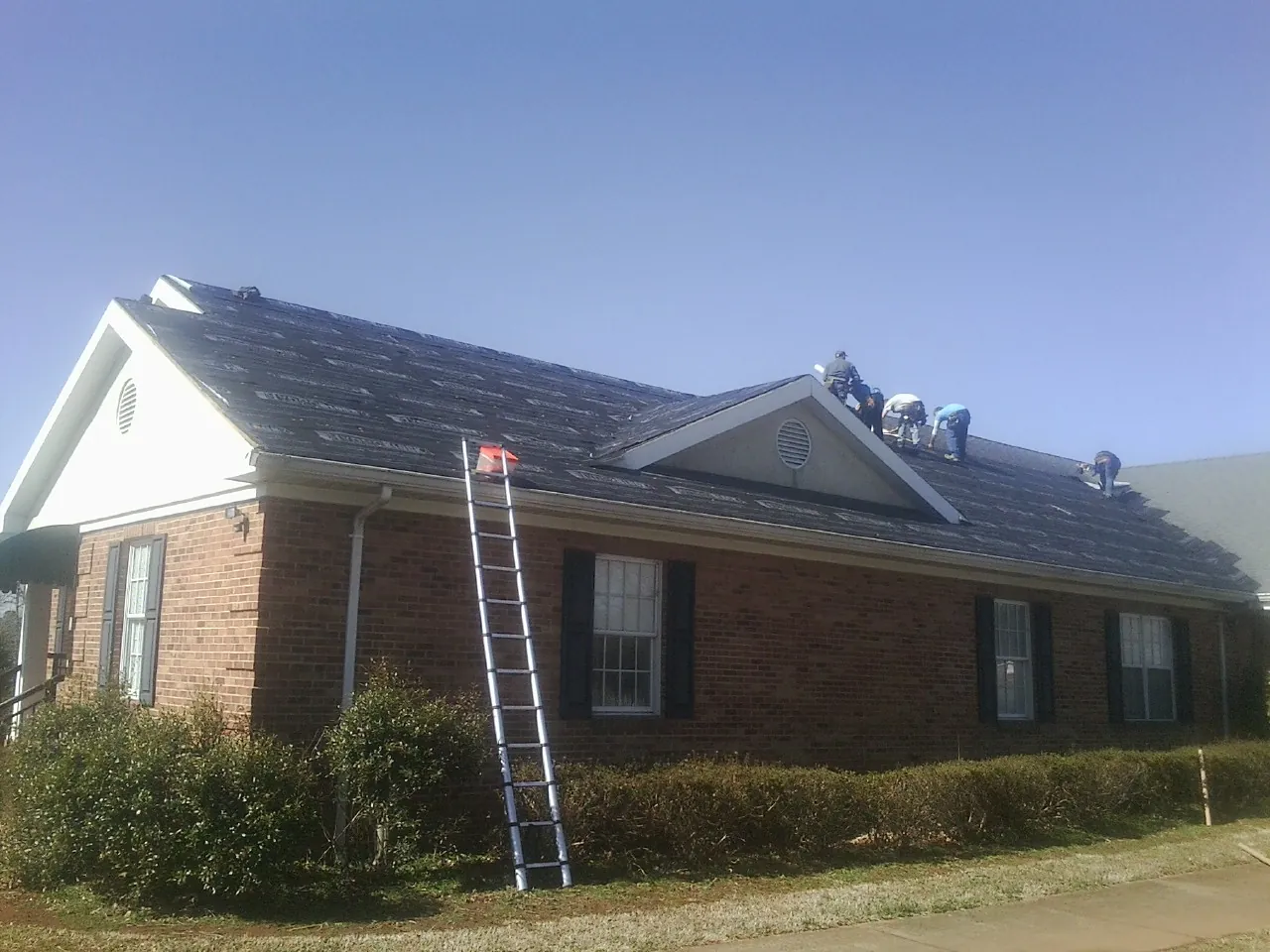 Crew tearing shingles off a brick ranch roof with a ladder set — Emergency Roof Repair work by our crew in Lake Junaluska