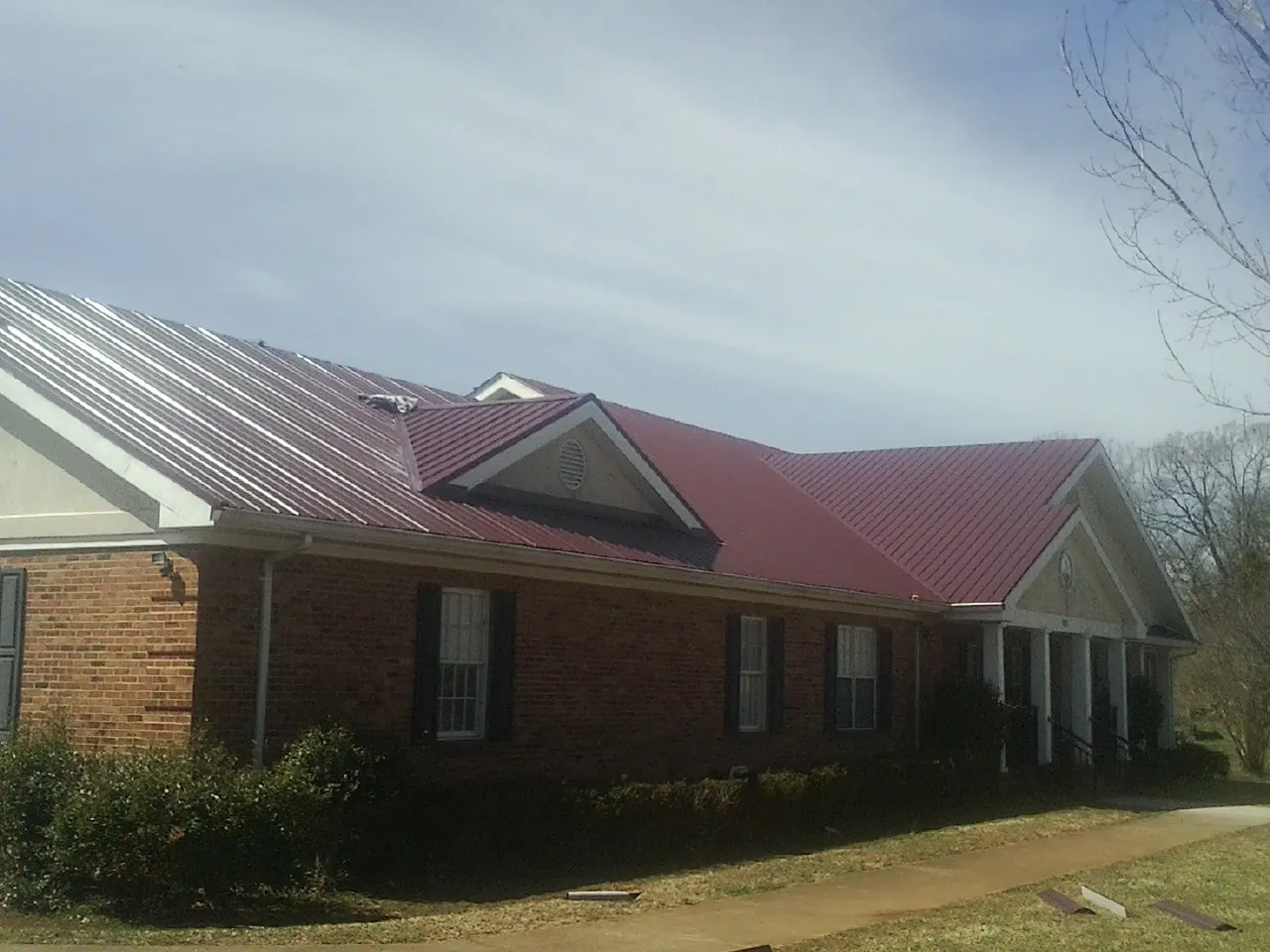 Red metal roof with gabled entries on a long brick building, from a Hail Damage Roof Repair job in Lake Junaluska