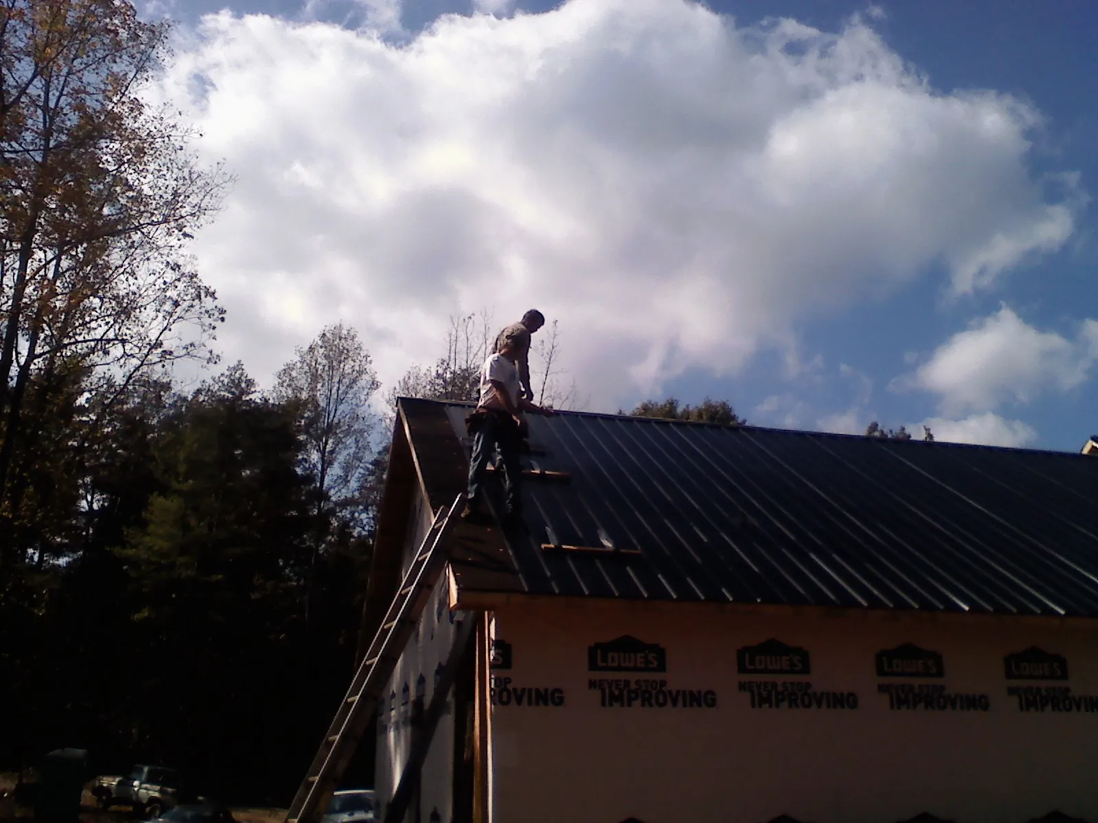 Roofer fastening dark metal panels high against a cloudy sky, from a Roof Inspection job in Lake Junaluska