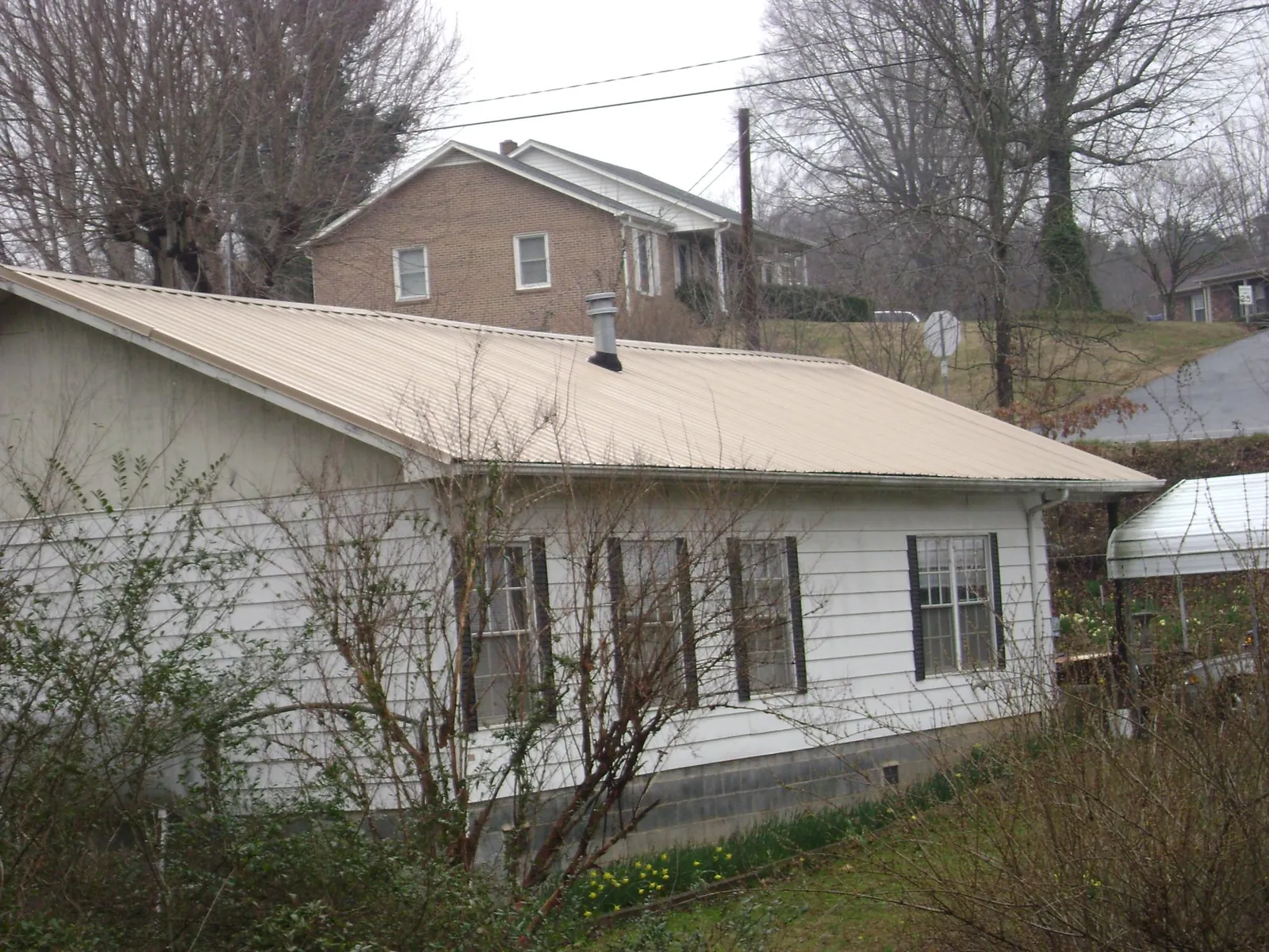 Tan metal roof on a white sided house set into a hillside — Commercial Roofing by Roofing Brothers in Lake Junaluska