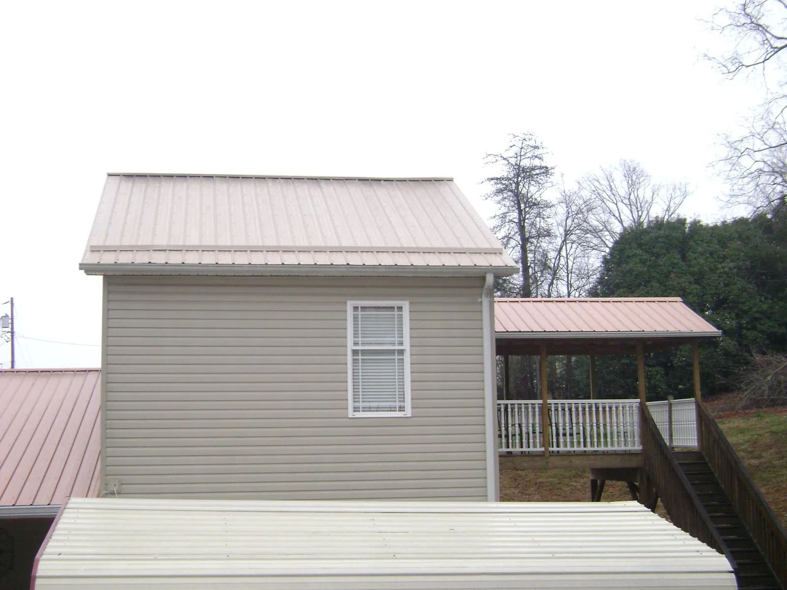 Tan metal roofs on a two story addition and attached porch, from a Roof Replacement job in Lake Junaluska